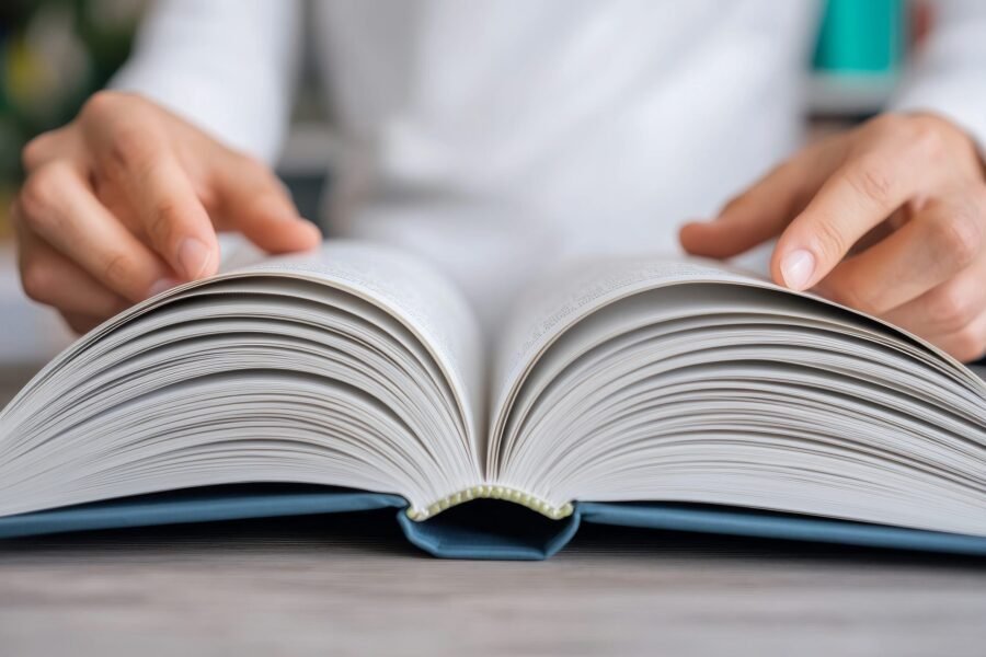 Open book with hands turning the pages on a wooden surface.