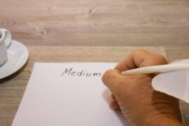 A person writing on a piece of paper next to a cup of coffee